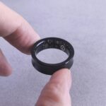 AI 기반 건강 관리, 개인 맞춤형 솔루션으로 헬스케어의 미래를 연다 Fingers hold a black smart ring with circuits visible.